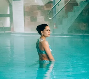 Mujer en piscina termal techada mirando al horizonte, reflejo celeste del agua Termas Aguas Calientes